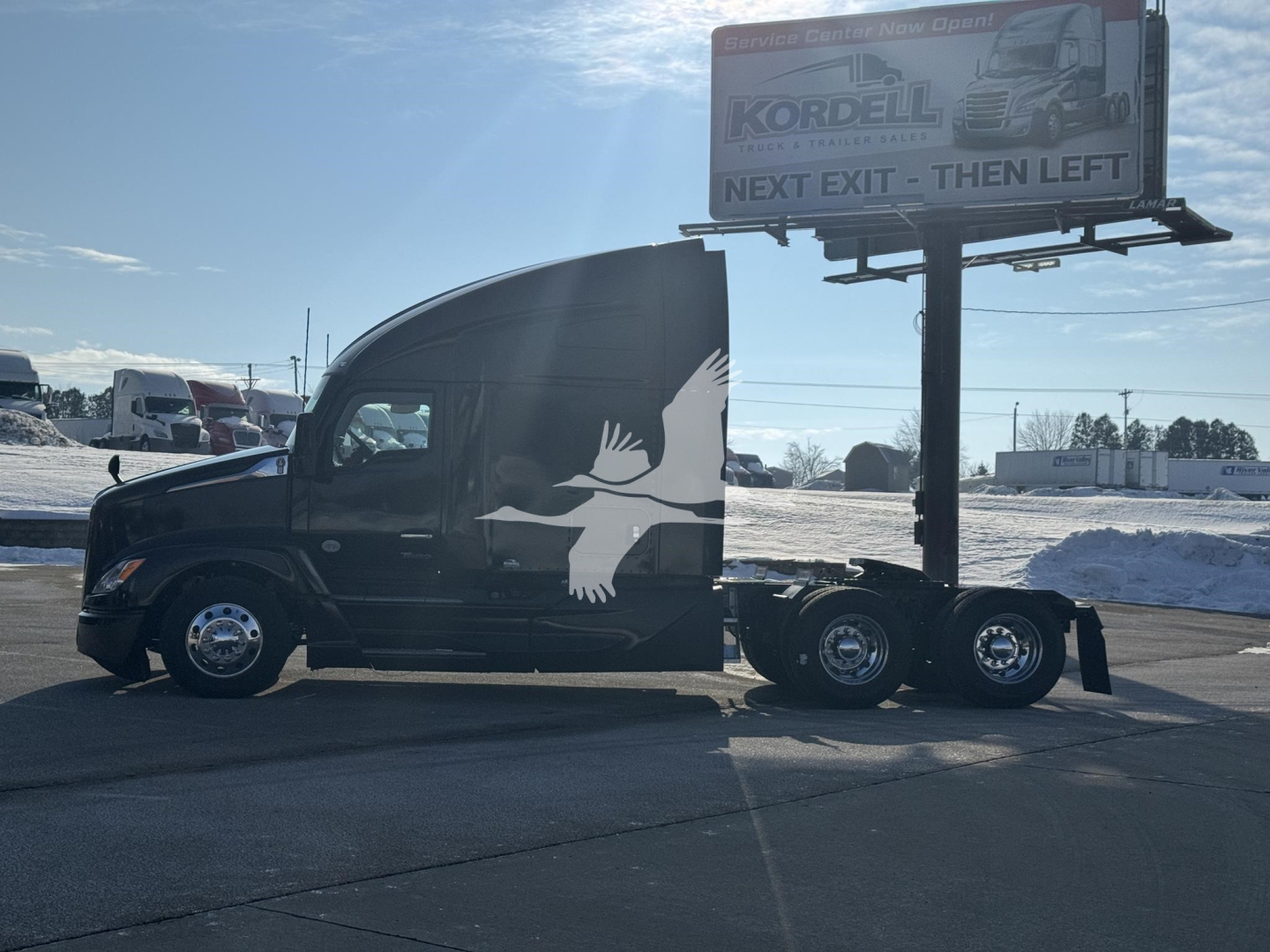 Truck cab and attached trailer with black paint and white eagle graphic. Billboard in background. Side view shows Kenworth T680 style sleeper cab.