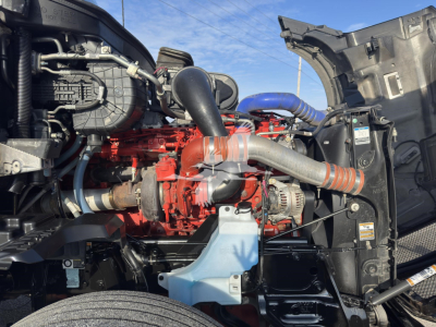 Kenworth T680 engine bay with red engine, blue coolant reservoir, silver exhaust ducting, and black surrounding components.