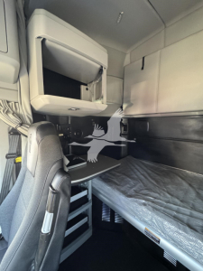 Kenworth T680 sleeper cab interior showing bunk bed area, storage cabinet, and desk with drawer unit.
