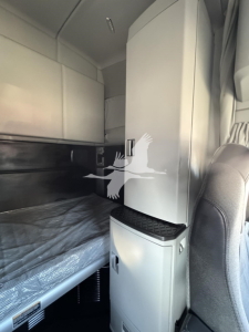 Cab interior of a 2022 Kenworth T680 sleeper with bunk bed and vertical storage cabinet.