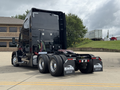 Kenworth T680 tractor rear view showing dual rear axles and fifth wheel area with bumper, shows black glossy cab and rear mud flaps.