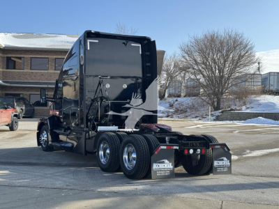 Kenworth T680 tractor rear view showing triple rear axles, black glossy exterior, mud flaps with Kordell dealer text, and winter scene.