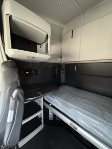 Kenworth T680 sleeper cab interior showing bunk bed, storage drawers, and overhead cabinet.