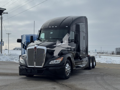 Kenworth T680 tractor-trailer in black, front view with sleeper cab; no visible text on the vehicle, snow on ground.