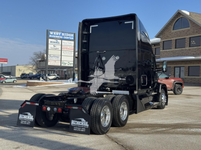 Kenworth T680 tractor rear/side view showing twin rear axles and mud flaps, black cab, registration signs in background.