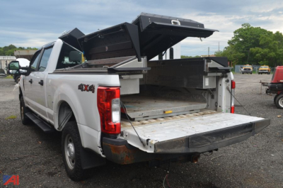 Ford F-250 Super Duty pickup truck in a salvage yard with open bed and hydraulic dump bed tailgate raised, showing rear cargo area and 4x4 badge.