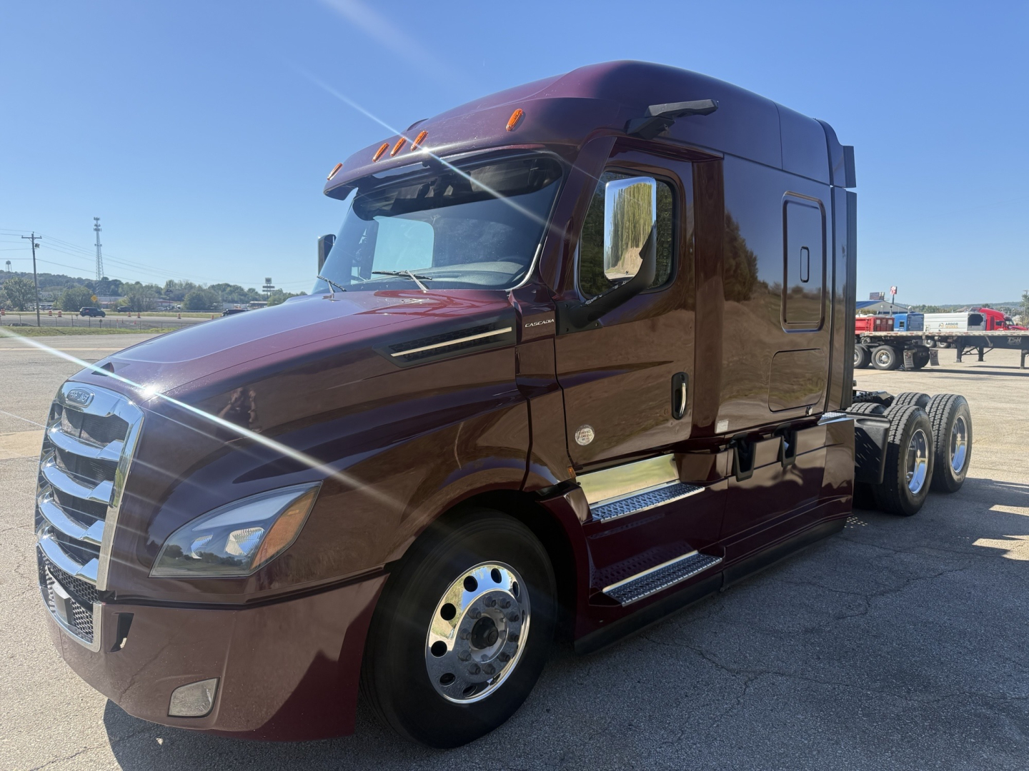 Freightliner Cascadia 126 tractor in maroon showing side view with sleeper cab and dual rear axles.