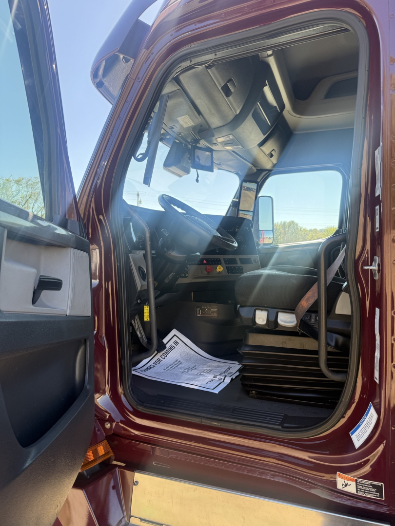 Cab interior of a Freightliner Cascadia 126 truck showing driver seat, dashboard, and steering column from an open door.