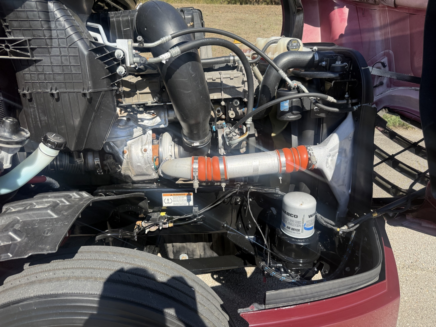 Freightliner Cascadia126 engine bay showing air intake tube, coolant reservoir, fuel filter canister, and various hoses; components visible in front area under hood.
