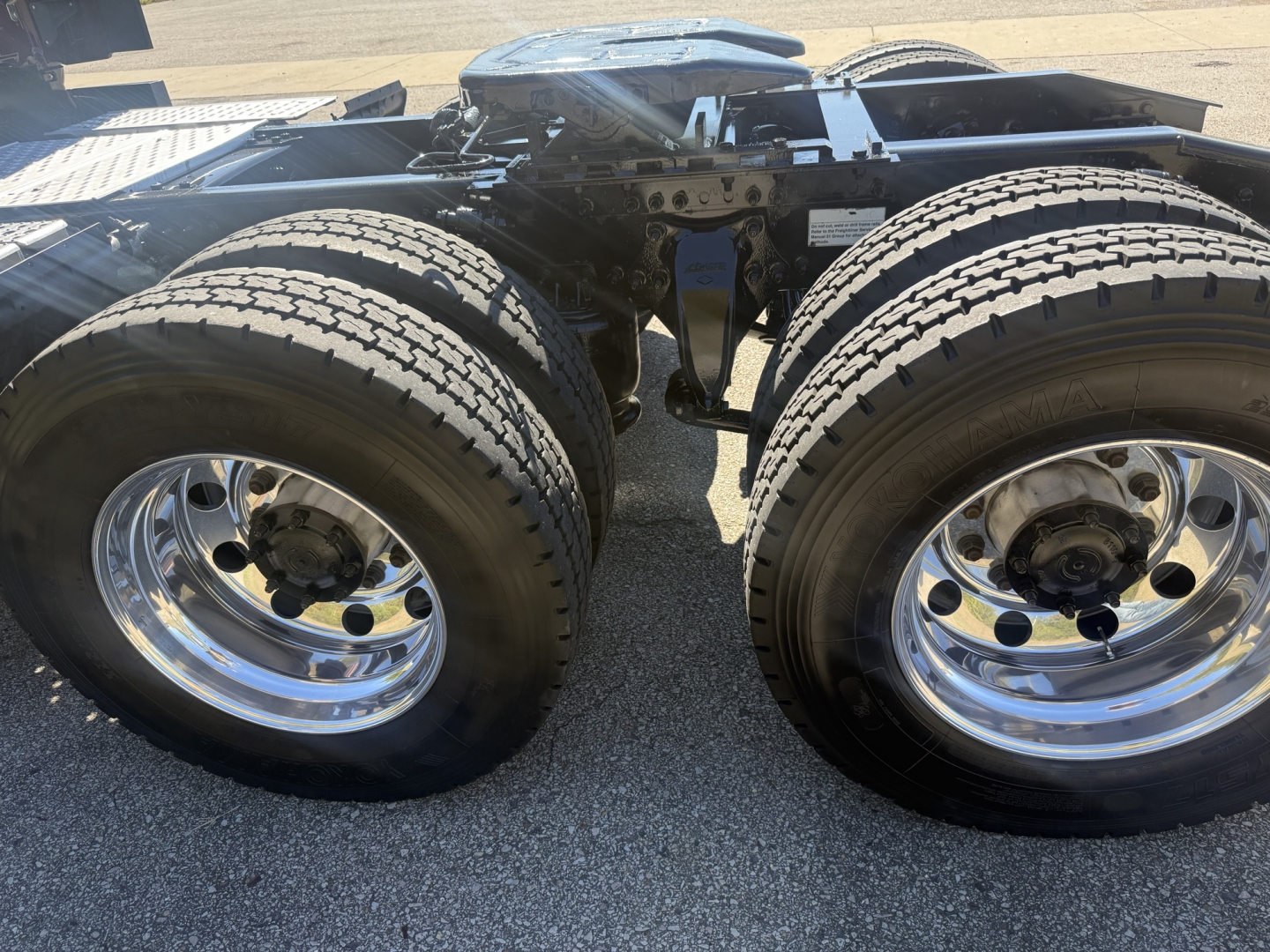 Dual rear axles with chrome wheels and tires on Freightliner Cascadia 126 chassis; view of fifth wheel and frame rails.