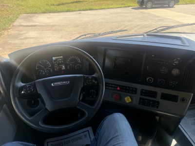 Truck interior of a 2021 Freightliner Cascadia 126, steering wheel, dashboard with gauges, center console, and control buttons visible.