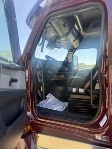 Cab interior of a Freightliner Cascadia 126 truck showing driver seat, dashboard, and steering column from an open door.