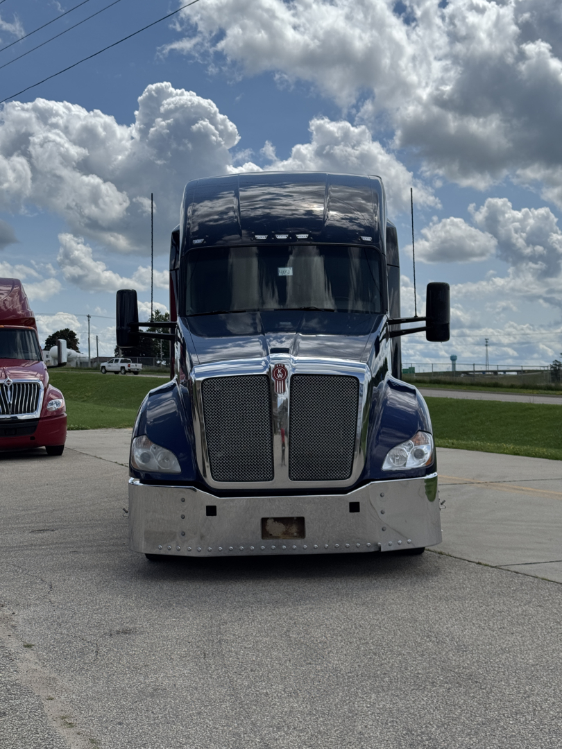Kenworth T680 front view showing chrome grille, large bumper, and dual side mirrors in blue with clear sky background.