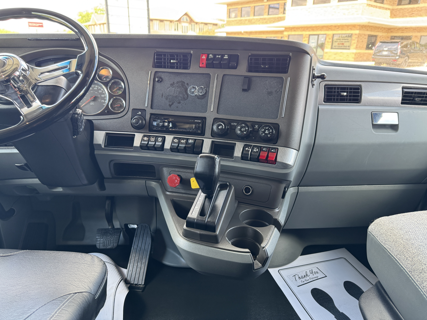 Cab interior of a 2018 Kenworth T680 with steering wheel, instrument cluster, center console, gear shifter, and dashboard controls visible.