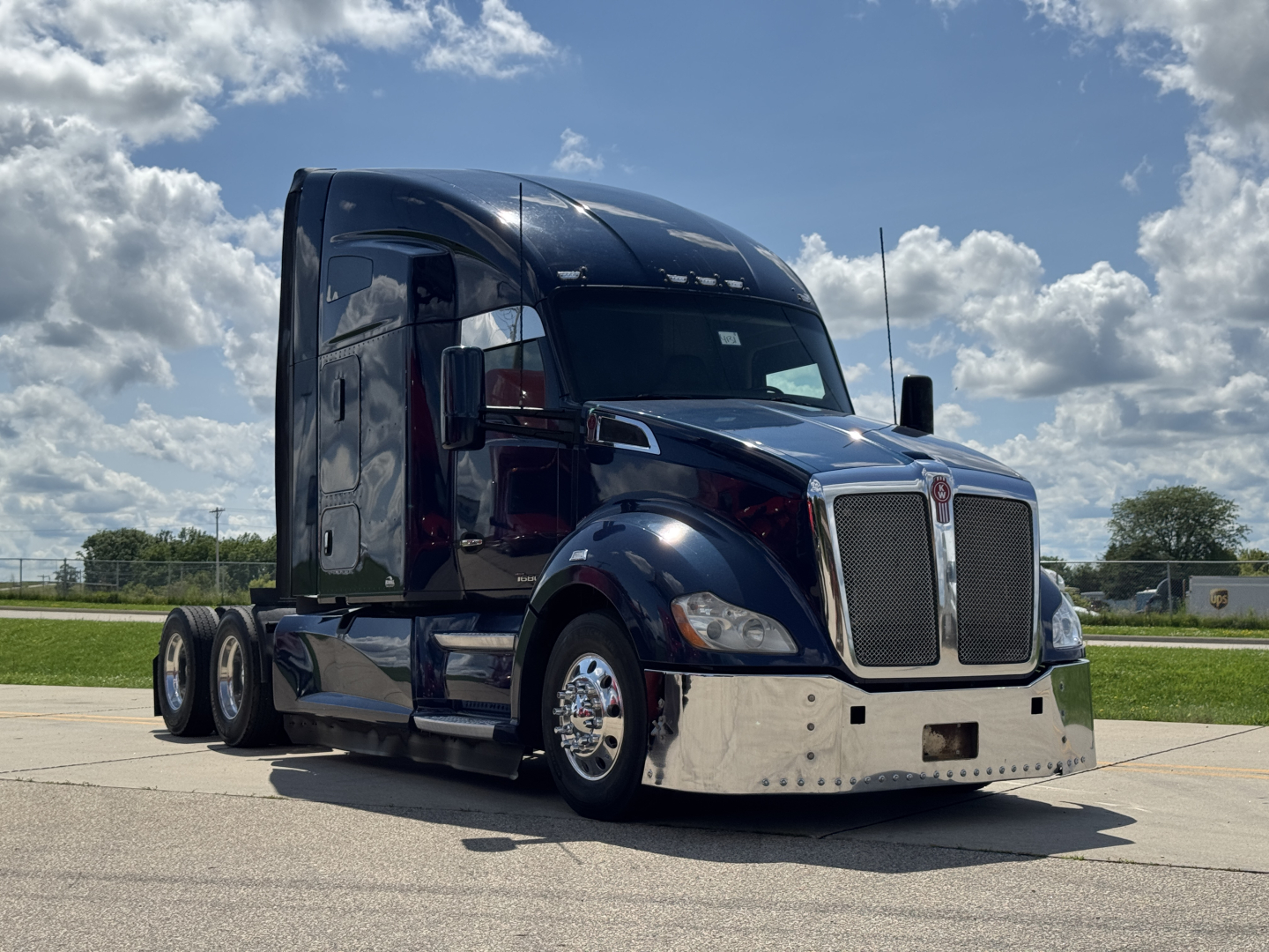 Kenworth T680 tractor unit in black with sleeper cab, chrome grille, polished bumper, side mirrors, and dual rear axles; daytime sky with clouds.