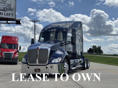 Kenworth T680 tractor-trailer in blue, front view, chrome grille and bumper, large windshield, power lines and a red truck in background.