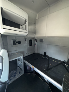 Kenworth T680 sleeper cab interior showing storage cabinet, wall panels, and sleeper bed platform with straps.