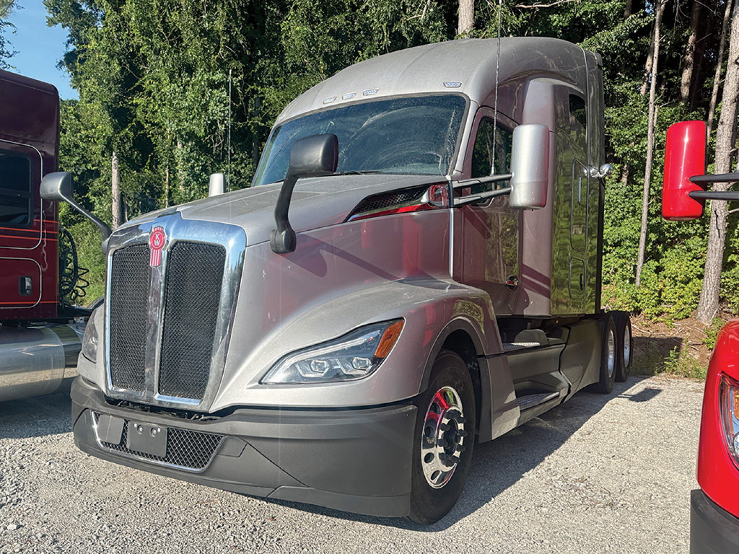 Kenworth T680 Next Gen tractor truck in a lot, front-left view with silver body, large grille, dual mirrors, and sleeper cab.