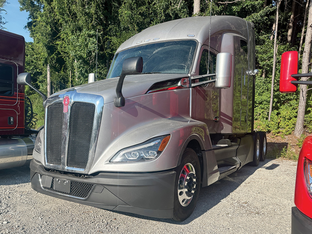 Kenworth T680 Next Gen tractor truck in a lot, front-left view with silver body, large grille, dual mirrors, and sleeper cab.