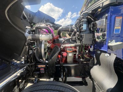 Engine bay of a 2027 Mack PI64T conventional daycab showing engine components, hoses, belts, and wiring.