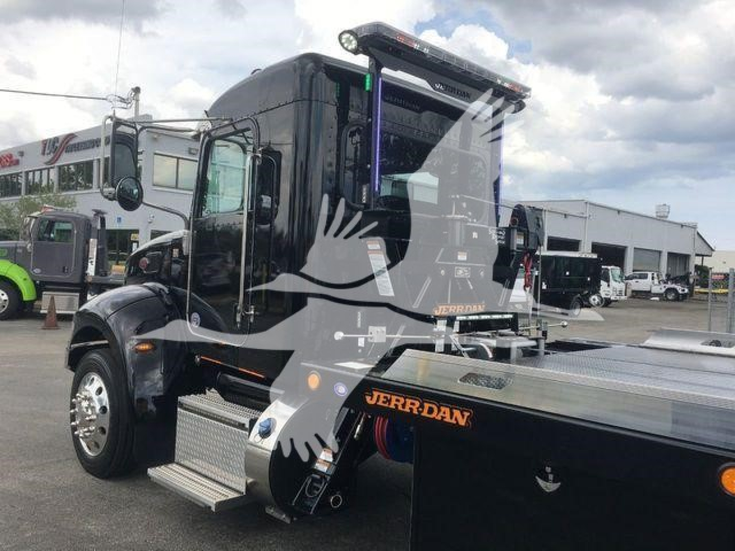 Truck hood and cab of a 2022 Peterbilt 337 tow truck with a JerrDan rollback bed, black exterior, chrome wheels, and side steps visible.