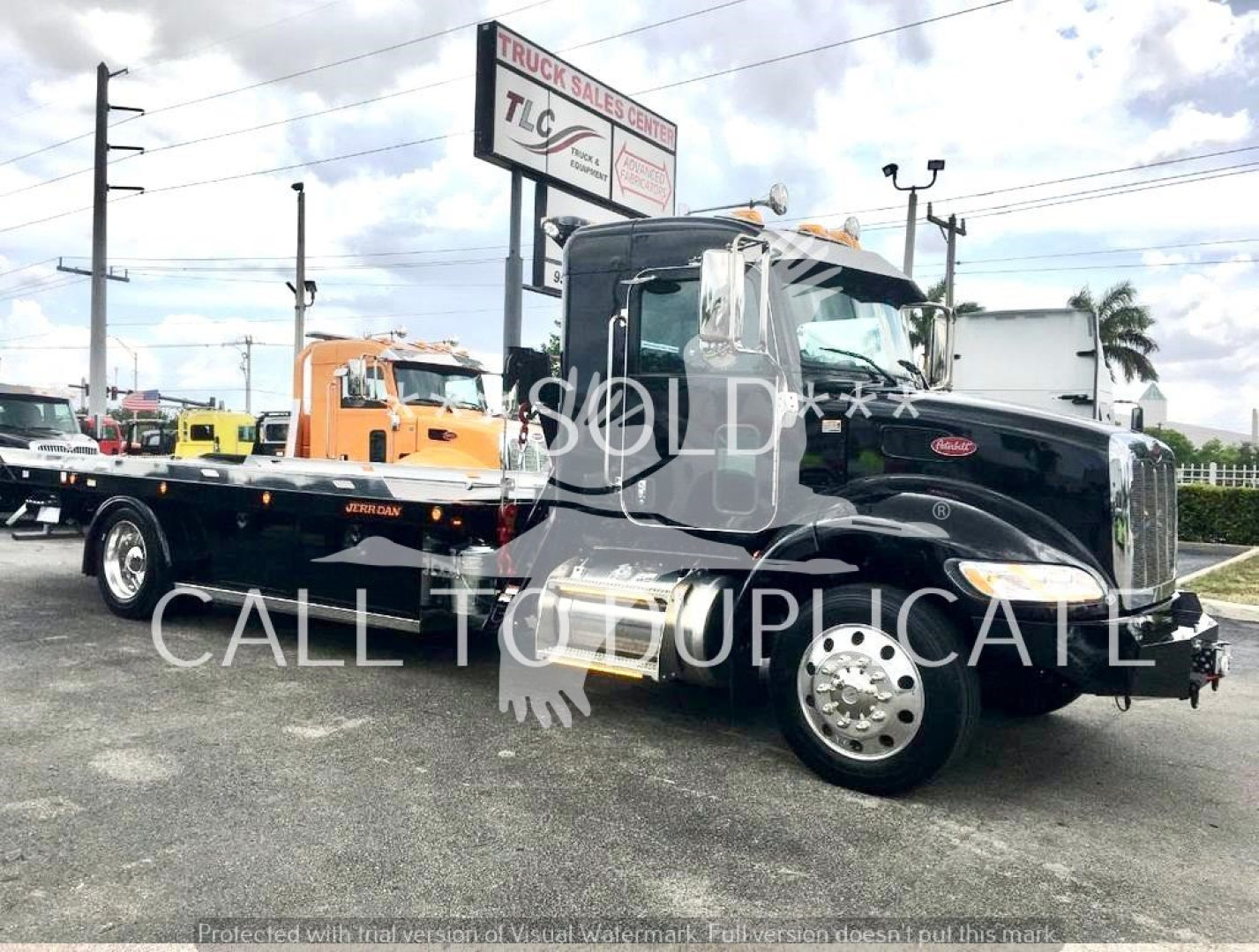 Peterbilt 337 truck in showroom/lot, black cab with rollback flatbed trailer attached, fuel tanks visible, signage in background, watermarked SOLD text.
