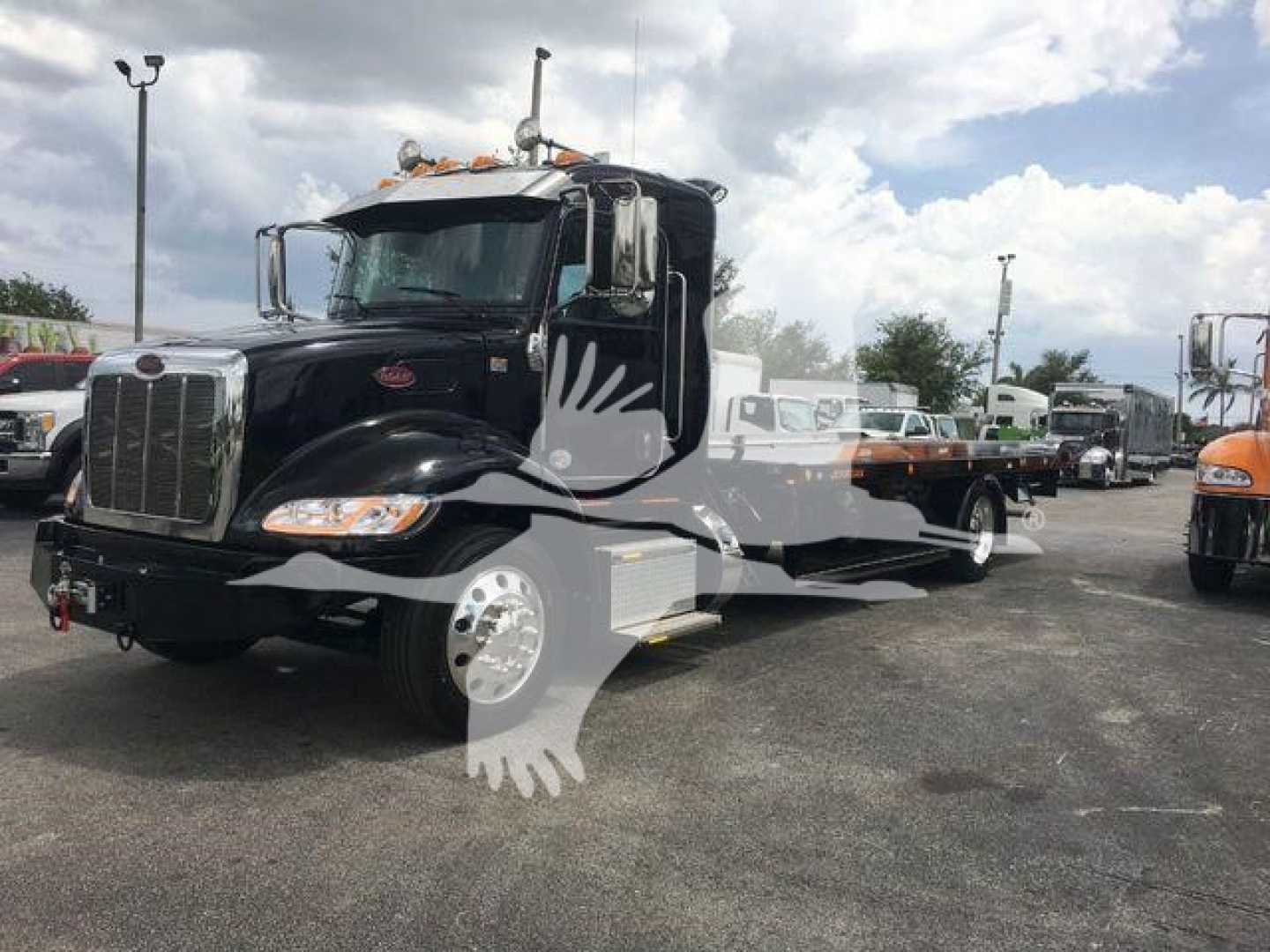 Peterbilt 337 rollback truck in a dealership lot, black cab with chrome grille, long bed, white wheel covers, side steps, and stacked exhaust on the passenger side.