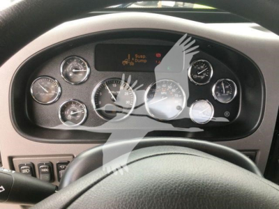 Peterbilt dashboard gauges and instrument cluster visible through steering wheel. Multiple circular gauges with needles; central digital display shows icons. Overlay watermark of a handprint graphic partially covers the panel.