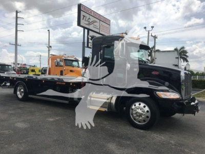 Peterbilt 337 rollback truck in service bay with extendable flatbed, black cab, chrome wheels, and a white lettered logo on the door.
