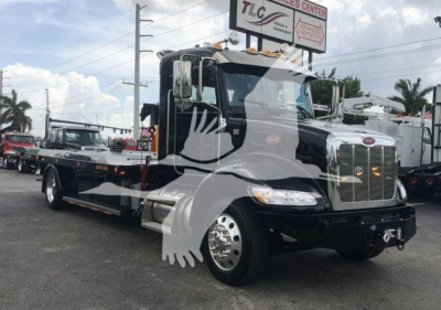 2022 Peterbilt 337 rollback wrecker chassis front angled view showing chrome grille, headlights, and black cab with white decals.