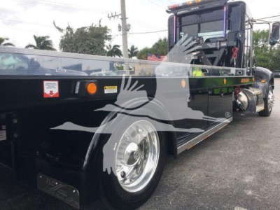 Peterbilt 337 rollback truck with a flatbed, side view showing front wheel and cab back detail.