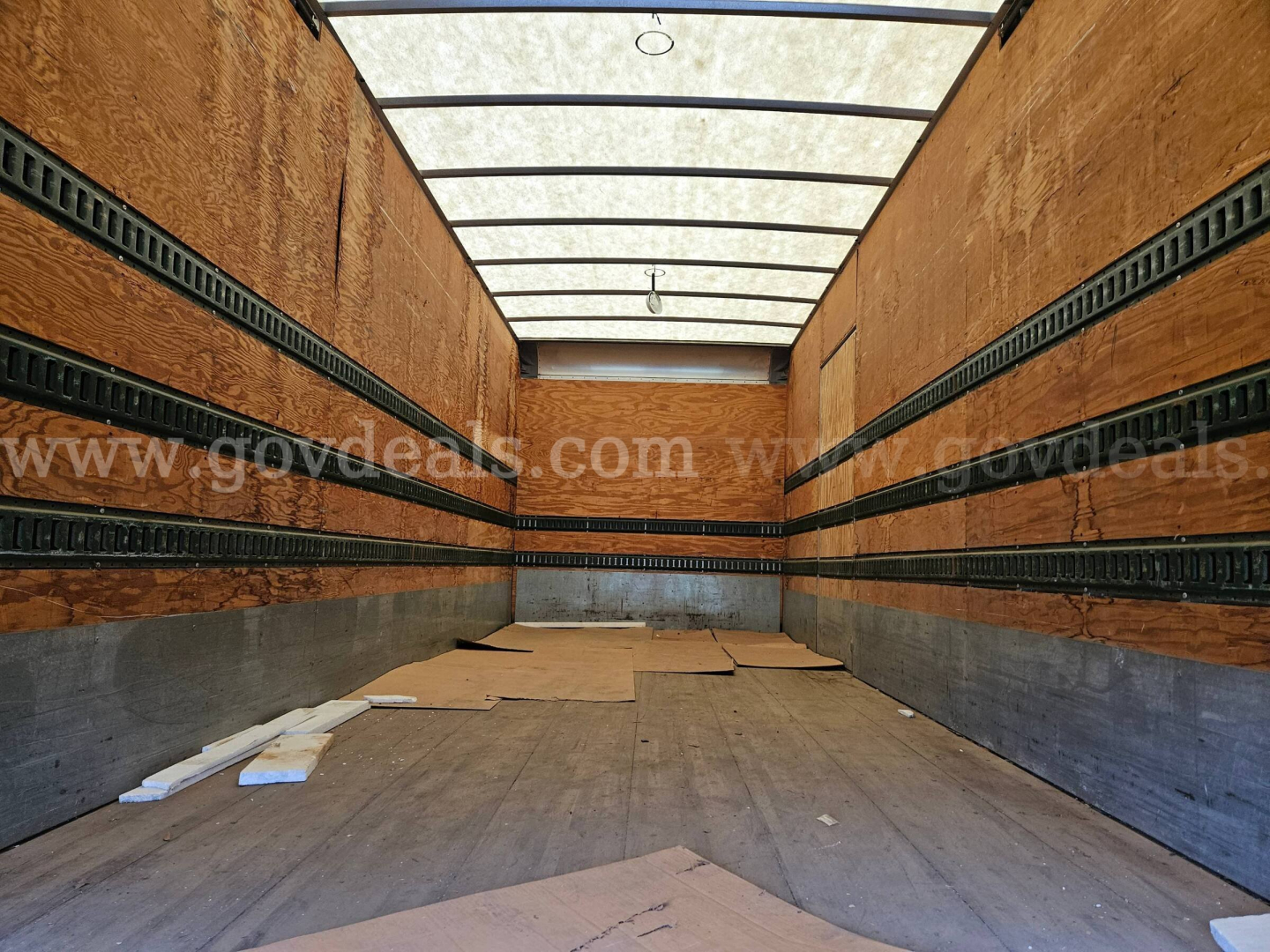 Truck cargo area of a 2003 Sterling Acterra box truck interior with wooden side walls and metal rails, empty floor with some debris.