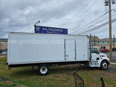 Box truck with white cab and large white cargo box, stock number 32136-61, parked on grass; sign in background reads 'GOV DEALS' and 'ACUITO' (partial).