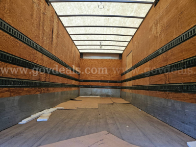 Truck cargo area of a 2003 Sterling Acterra box truck interior with wooden side walls and metal rails, empty floor with some debris.