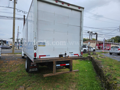 Rear view of a white Sterling Acterra box truck with closed cargo doors and a rear bumper/step, parked on grass by curb.