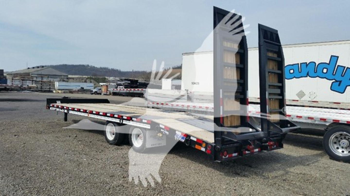Flatbed trailer on a lot with ramps raised at the rear and trailer tires visible, dealership yard in background.