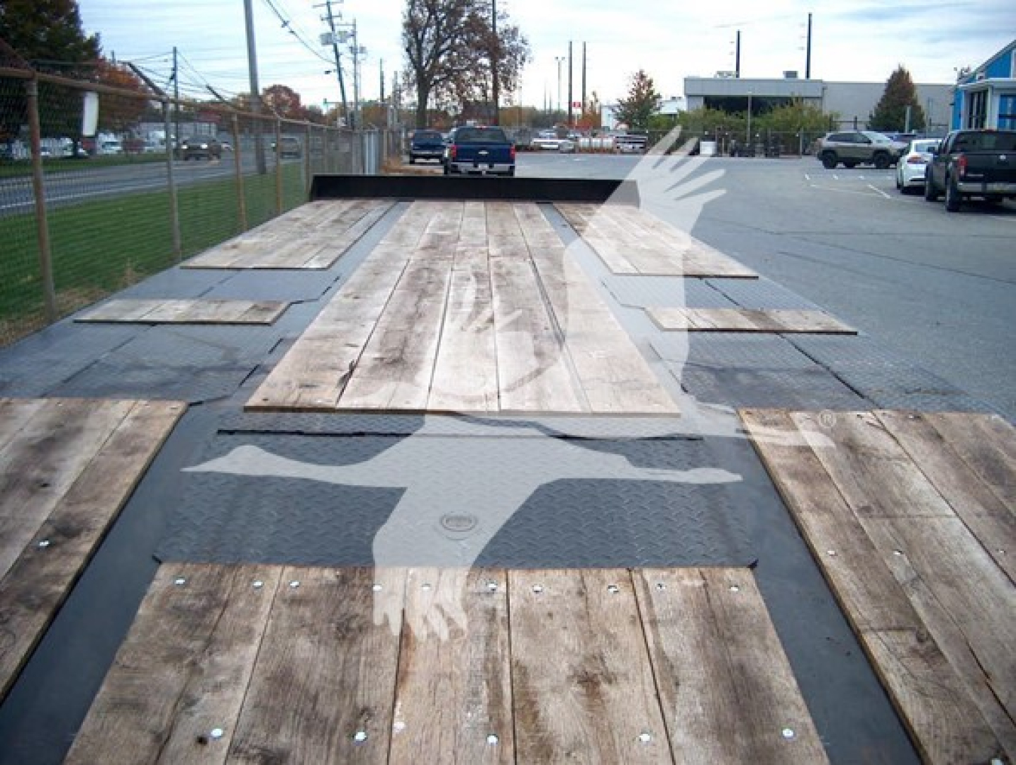 Flatbed trailer deck with wooden planks and steel step for loading, viewed from the rear toward the cab, logo of a white eagle on the deck.