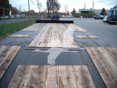 Flatbed trailer loading deck with wooden planks and black metal frame, rear view showing a hand silhouette graphic and reflective surface.