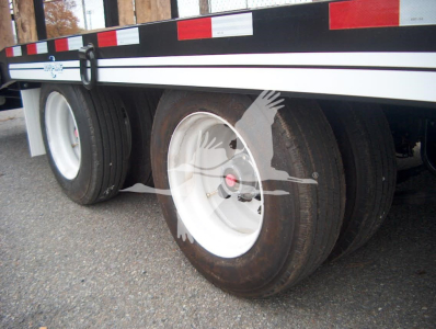 Trailer with dual rear axles and white wheel rims showing tires and side railing. visible text includes VIN and stock number area.