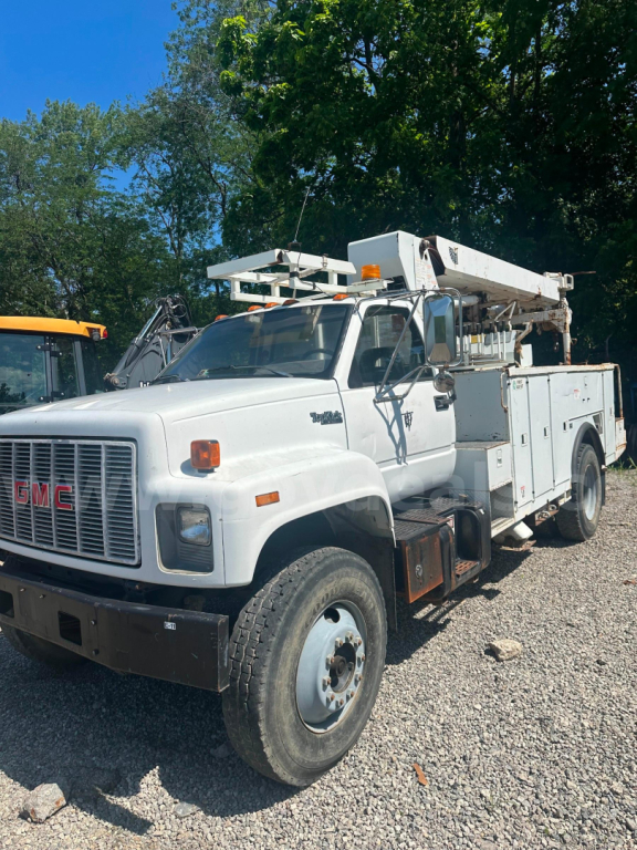 GMC boom truck in service showing utility body and bucket crane with white exterior and black bumper.