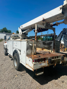 Boom truck rear view showing weathered white utility body with rust on flatbed and stabilizing booms, rear lights, and bumper.