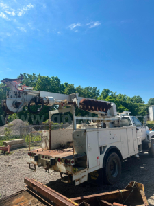 Boom truck rear and crane arm on utility truck with white body and metal rack, visible coil and hoses.