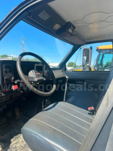 GMC truck cab interior showing steering wheel, dashboard, and driver seat; visible window and side mirror; some controls on the dash.