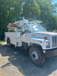 Truck chassis showing boom lift utility service body with electrical controls and hydraulic lines.