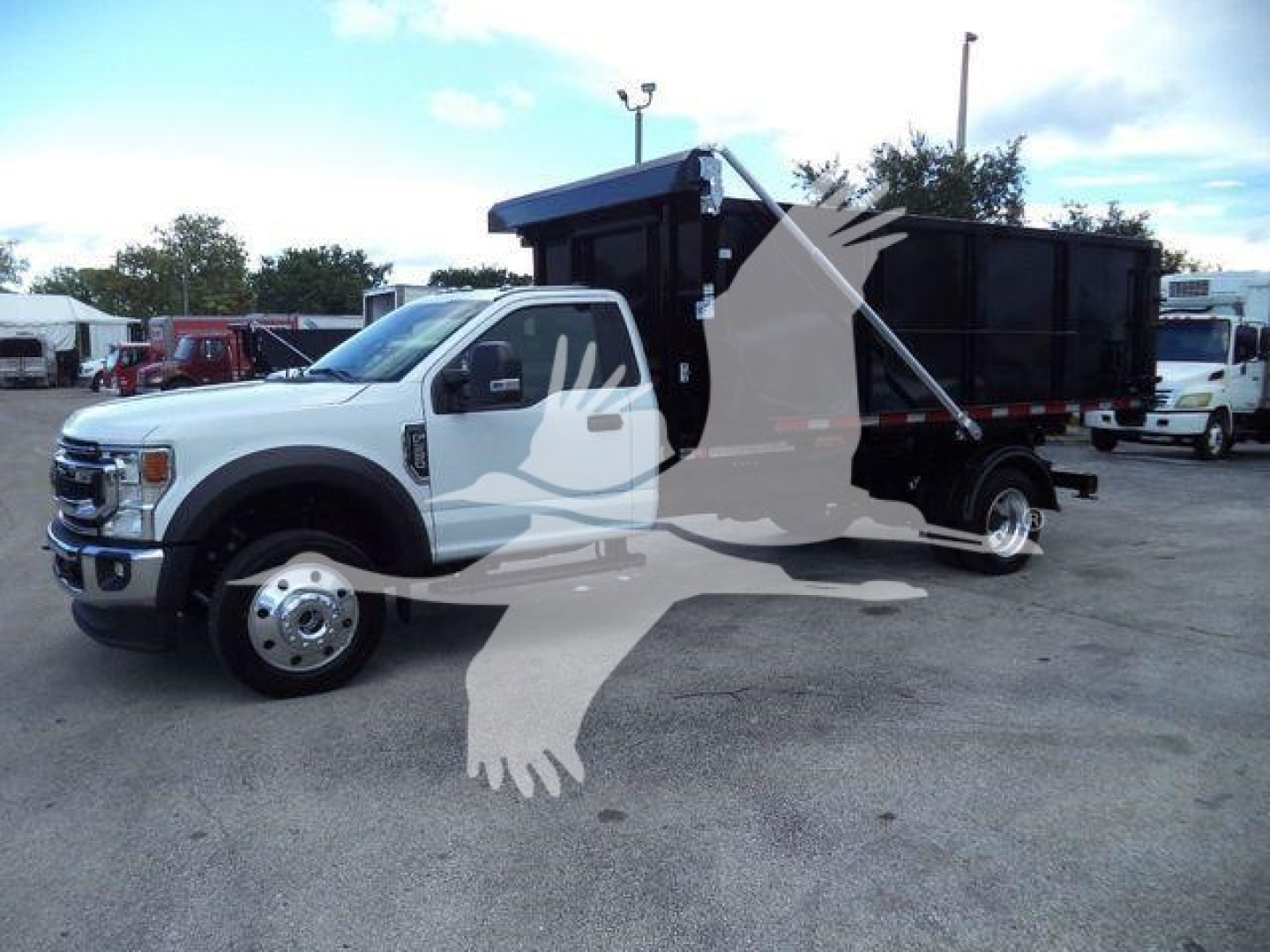 Ford F-550 rolloff truck with black dump bed and white cab, side view showing front grille and wheel, stock label in background