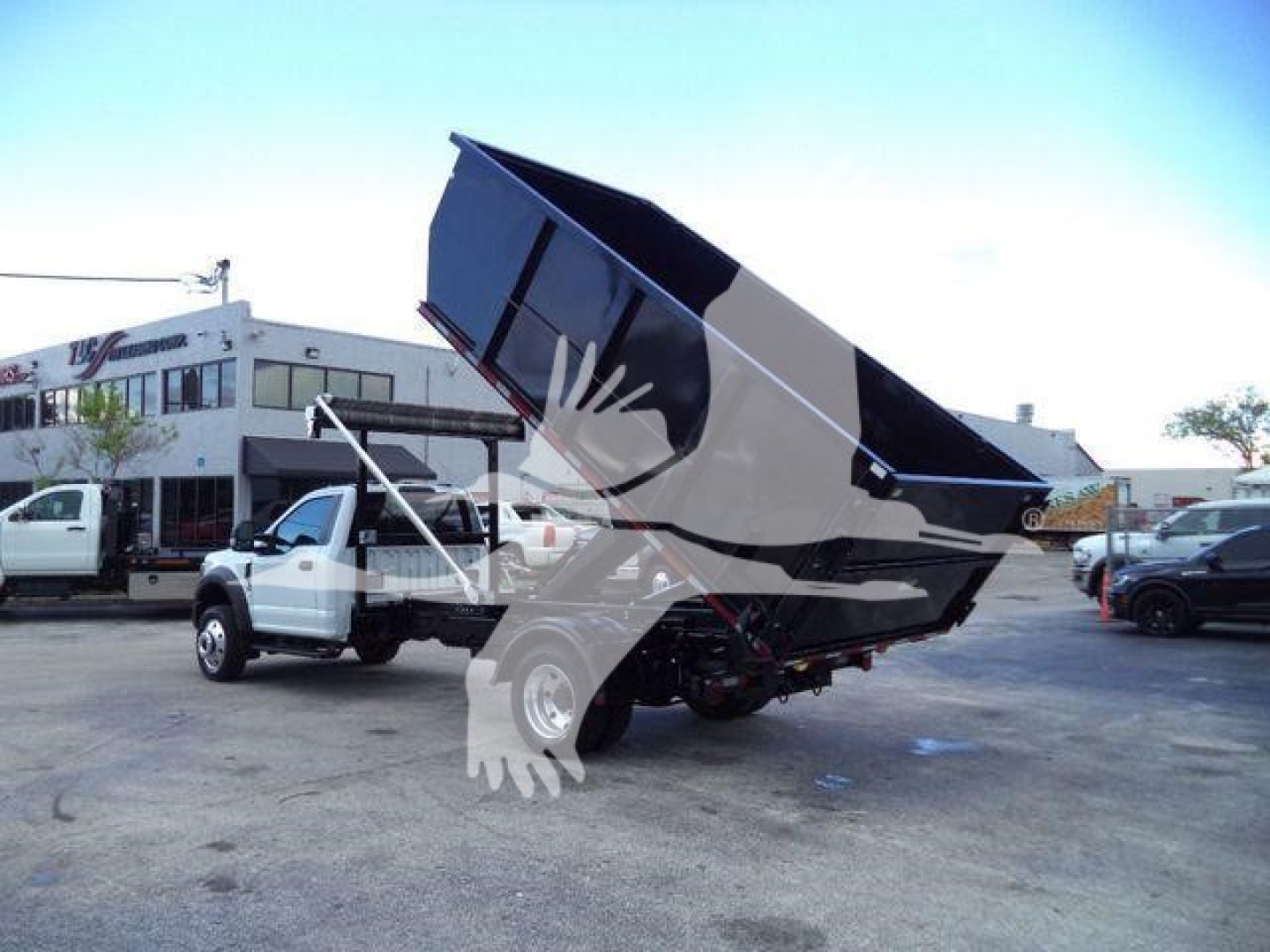 Ford F-550 roll-off truck with raised dump bed in a dealership lot, side view showing front cab and chassis