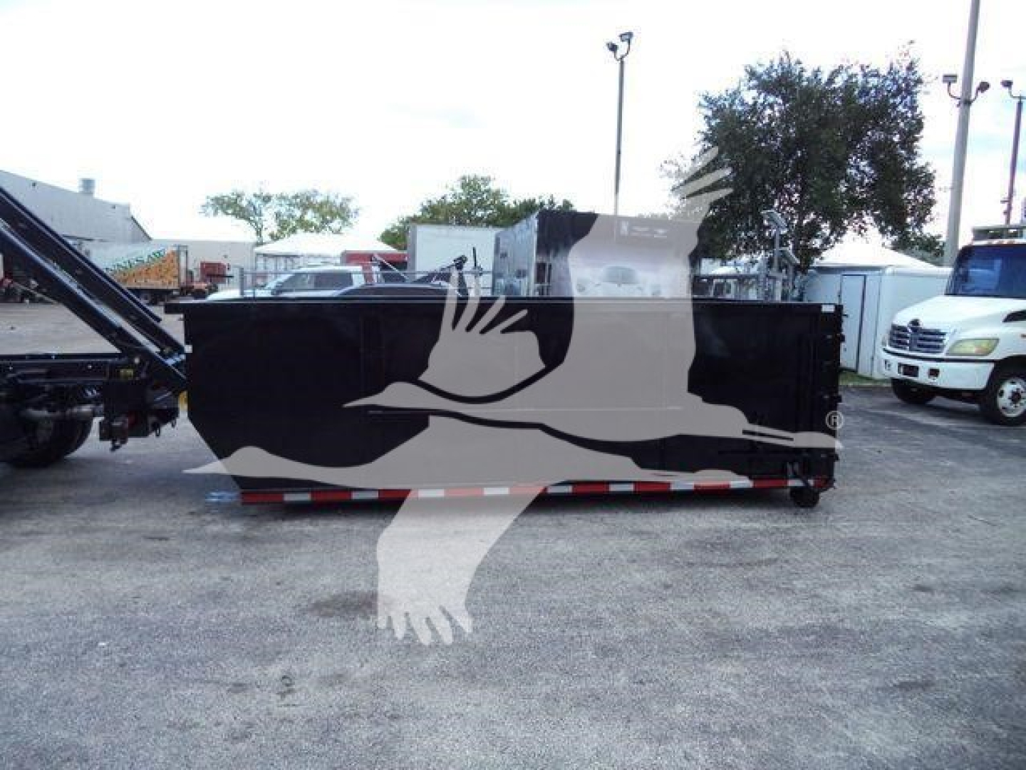 Ford F-Series roll-off truck body with black exterior and red/white reflective trim, stock number F550GAS14SNG4X4, in a lot.