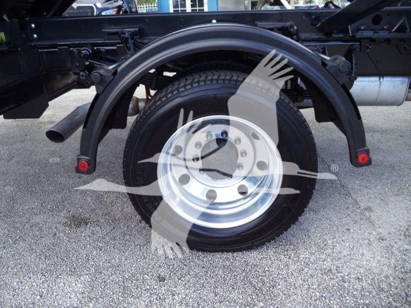 Wheel assembly showing tire and spare wheel with fender arches and suspension components of a Ford F-550 roll-off truck.