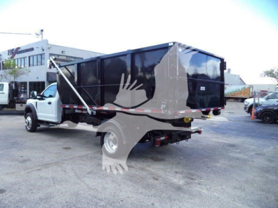 Ford F-550 roll-off truck with a large black dumping bed, side view showing white cab and 4x4 configuration.