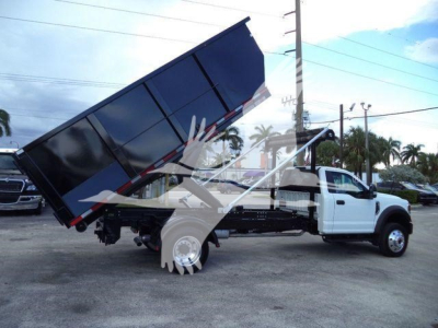 Ford F-550 rolloff truck with dump bed raised, side view showing white cab and black dump body.